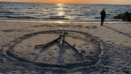 peace sign carved into the sand on a beach at low tide, sunset.