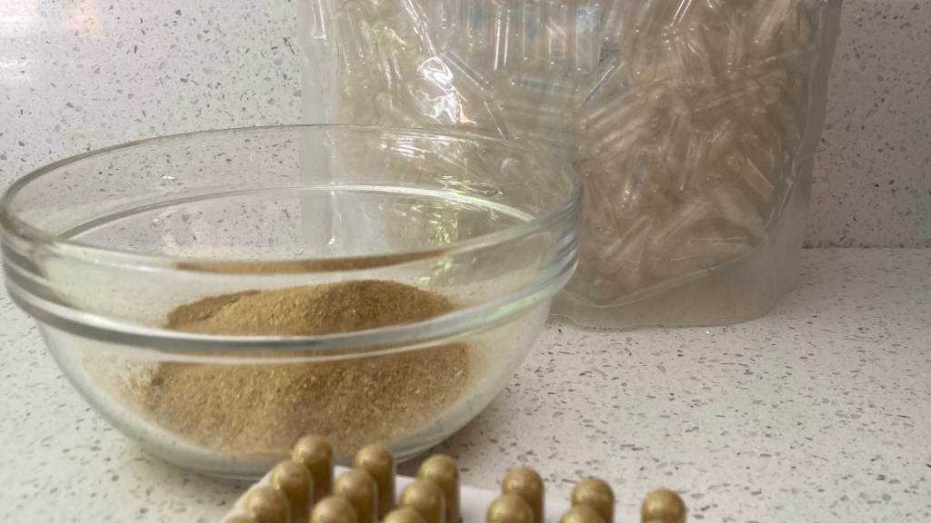 capsules in a capsule maker, a bowl of powdered herbs, a bag of vegan gelatin capsules